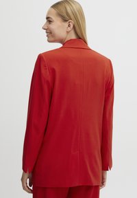 Blazer su misura rosso con silhouette strutturata, dotato di colletto a pistagna e una fessura posteriore singola. Tessuto liscio con dettagli minimi.