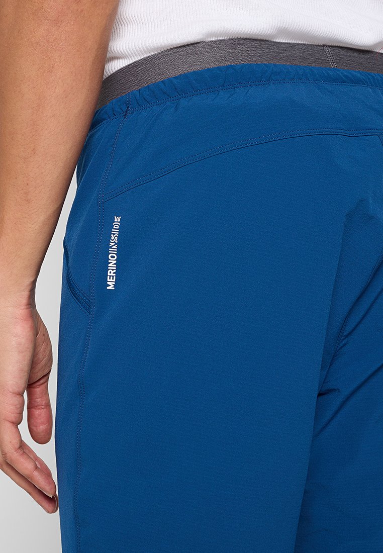 Gros plan sur une personne portant un short MerinoMix bleu et un t-shirt à côtes blanc, en se concentrant sur la zone de la poche latérale et de la taille.