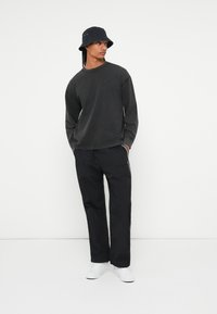 Crna dugotrajna majica s okruglim izrezom, u kombinaciji s crnim hlačama s bočnim trakama, dopunjena tamnim šeširom u obliku kante i bijelim cipelama.