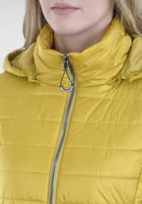 Gelbe gepolsterte Jacke mit hohem Kragen, Reißverschluss und Logo-Reißverschlussanhänger. Das Material hat eine glatte Textur mit horizontaler Steppung.