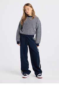Navy striped sweater with ribbed cuffs and hem, paired with loose-fitting dark navy pants featuring white side stripes and sneakers.