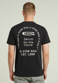 T-shirt noir G-Star Raw avec un texte au dos : "Denim pour l'avenir" et un logo de la marque. Manches courtes, coupe standard, en coton.