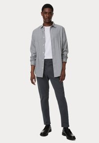 Grijs en wit gestreepte overhemd met knopen over een witte crewneck, gecombineerd met donkere getailleerde broek en zwarte schoenen. Eenvoudige, moderne uitstraling.
