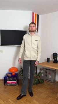 Ανοιχτό μπεζ φούτερ με φερμουάρ και υφή στα μανίκια, μαύρο λογότυπο, συνδυασμένο με σκούρο γκρι τζιν καμπάνα και σκούρα παπούτσια. Μινιμαλιστικό δωμάτιο με διακόσμηση.