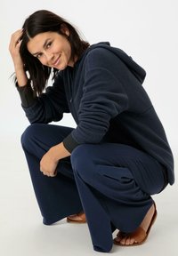 Navy-Fleece-Hoodie mit langen Ärmeln und Kapuze, kombiniert mit weiten, marineblauen Hosen und braunen Sandalen, im entspannten Schnitt und mit weicher Textur.