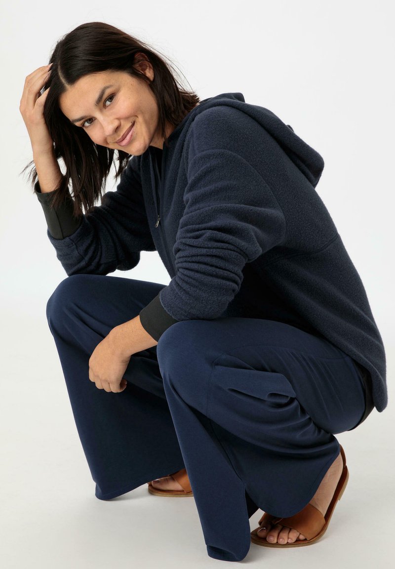 Navy-Fleece-Hoodie mit langen Ärmeln und Kapuze, kombiniert mit weiten, marineblauen Hosen und braunen Sandalen, im entspannten Schnitt und mit weicher Textur.