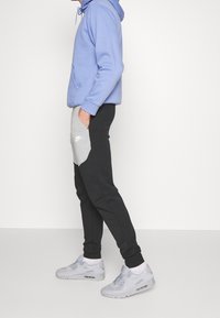 Ljusblå hoodie med en främre ficka, tillsammans med svarta joggers med en grå panel och Nike-logotyp. Grå sneakers fulländar outfiten.