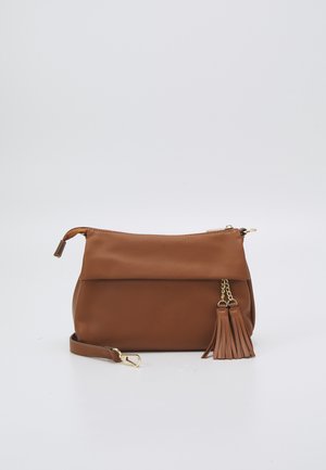 Petit sac bracelet en cuir marron avec fermeture éclair dorée, bandoulière détachable et deux pompons décoratifs sur un fond clair.