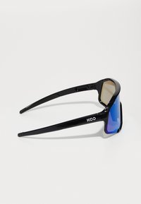 Black sunglasses with a wraparound design, featuring gradient blue lenses and logo detail on the arm. Sleek, smooth textures throughout.