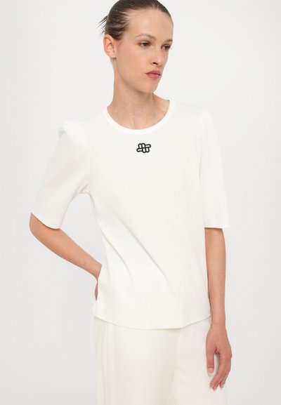 Top alb cu maneci scurte, cu textură ribbed, gât rotund și accent brodat negru la piept. Design simplu, ajustat.