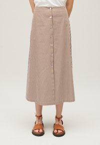 Brun och vit randig midikjol med knäppning framtill, resår i midjan och mjukt tyg. Kombinerad med bruna sandaler.