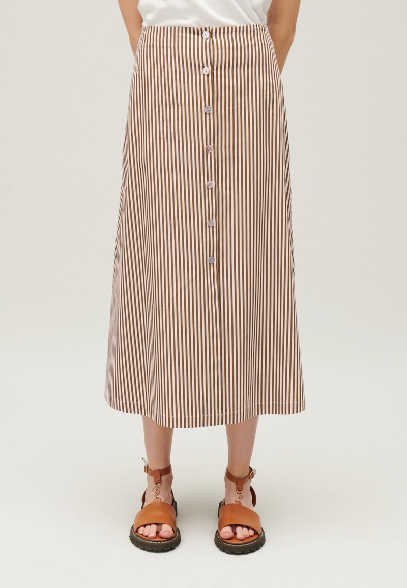 Brun och vit randig midikjol med knäppning framtill, resår i midjan och mjukt tyg. Kombinerad med bruna sandaler.