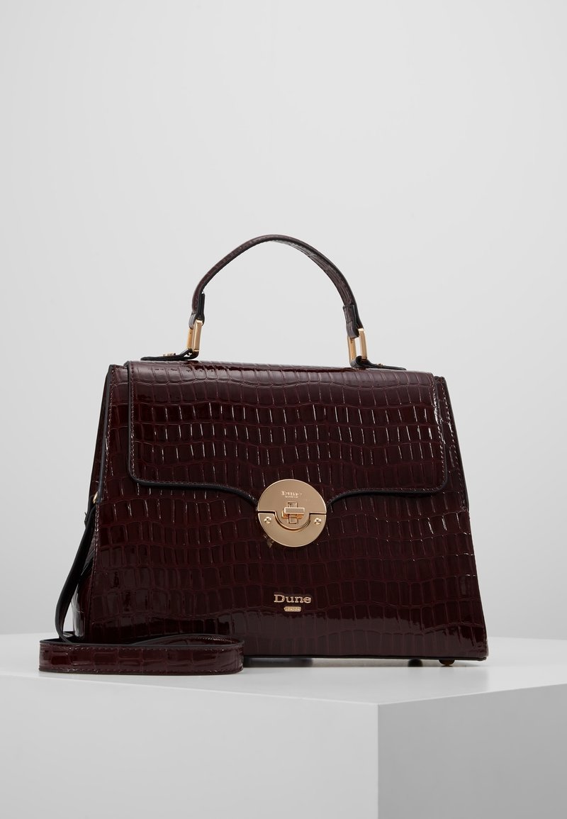Krokodilprickig bordeauxhandväska med ett guld cirkulärt lås, topphandtag och lång avtagbar rem. Slät textur, strukturerad design.