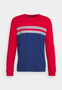 Camicia a maniche lunghe con un'area superiore rossa e due stripe grigie, e un fondo blu. Realizzata in cotone, presenta polsini a coste e un piccolo logo.