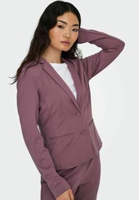 Lilla skreddersydd blazer laget av myk stoff, med notched krage, to-knappers lukking og frontlommer. Jevn tekstur, tettsittende design.