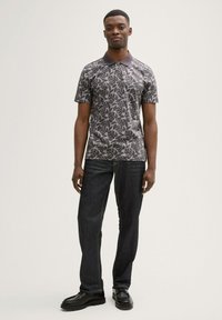 Polo de manga corta en gris oscuro con patrón de hojas, combinado con jeans de mezclilla oscuros y zapatos negros, con un cuello tipo polo.