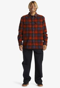 Rød og blå ternet flannel skjorte med to brystlommer, parret med løse sorte bukser og sorte sneakers.