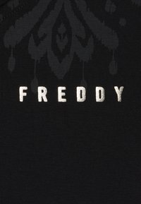Tela negra con un patrón texturizado y letras metálicas plateadas que dicen "FREDDY". La tela tiene una textura acanalada.