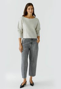 Pull en argent texturé avec un large col, associé à un jean en denim gris taille haute et des ballerines noires à bout pointu.