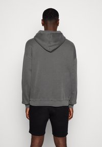 Harmaa hupullinen collegepaita, joka on valmistettu pehmeästä kankaasta ja siinä on rento istuvuus. Siinä on leveä huppu sekä resorireunukset hihoissa ja helmassa. Yhdistetty mustiin shortseihin.