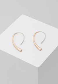 Boucles d'oreilles en métal avec un design courbé ; l'une en argent et l'autre en rose gold. Fini lisse, style minimaliste.