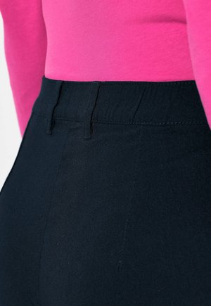Pantaloni neri a vita alta con una texture liscia e una cintura elastica, abbinati a un top rosa a maniche lunghe aderente visibile in vita.