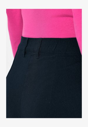 Zwarte broek met hoge taille, voorzien van een gladde textuur en een elastische tailleband, gecombineerd met een aansluitende roze top met lange mouwen die zichtbaar is bij de taille.