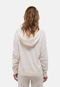 Sweat à capuche beige clair avec poignets et ourlet côtelés, en matière douce, présentant une coupe décontractée et un design minimaliste.