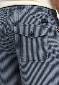 Shorts u mornim i svijetlosivim prugama s dugmadima na stražnjem džepu, koji imaju tkanu oznaku i teksturiranu tkaninu. Elastični pojas.