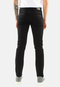 Jeans skinny neri con tasche posteriori e dettagli di cucitura distintivi, realizzati in denim, abbinati a sneakers grigie.