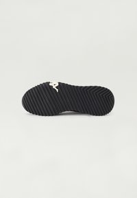 Suela de sneaker de goma negra con un patrón texturizado en zigzag, presentando un logo blanco en contraste. Bordes suaves y diseño de punta redondeada.
