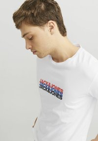 Witte katoenen t-shirt met meerkleurige "JACK & JONES" tekst in rood, blauw en zwart. Korte mouwen, ronde hals, gladde textuur.