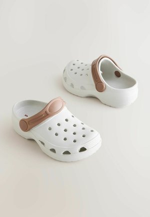 Sabots blancs avec une surface texturée, comportant plusieurs trous de ventilation et une sangle réglable marron sur le cou-de-pied.