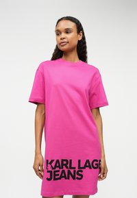 Vestido em algodão rosa com mangas curtas, apresentando um decote redondo e um grande logo preto "KARL LAGER JEANS" perto da bainha.