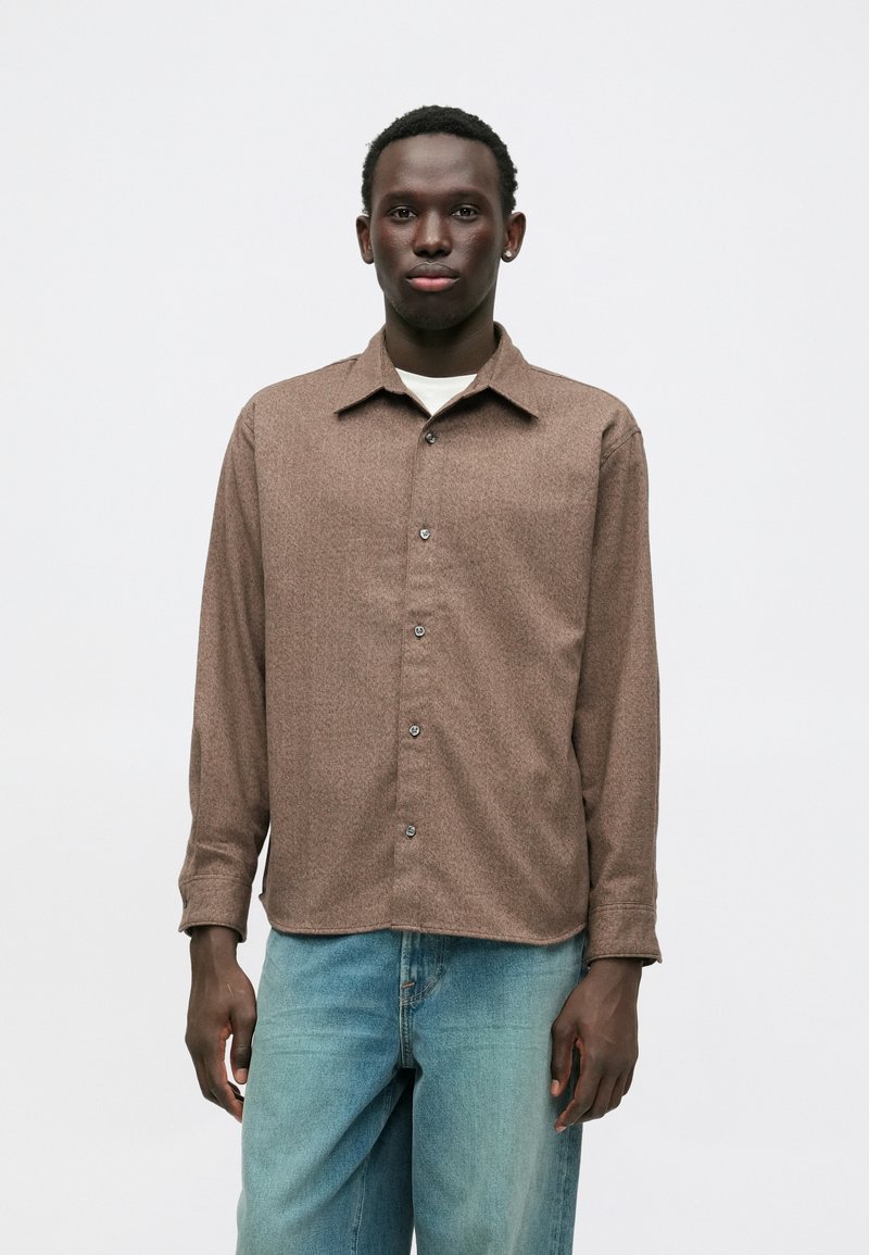 Καφέ πουκάμισο με σχέδιο, μακρύ μανίκι, κολάρο, κουμπάκι και μαλακή υφή, σε συνδυασμό με ανοιχτό μπλε τζιν παντελόνι.