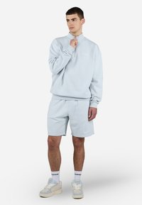 Lyseblå zip-up sweatshirt lavet af blødt stof, parret med matchende shorts. Har ribbede manchetter og en subtil logoaccent på brystet.