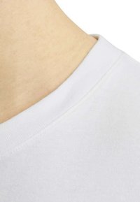 Camiseta de algodón blanca con cuello redondo, que presenta una textura suave y costuras reforzadas en el cuello.