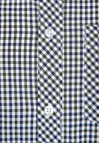 Camicia con bottoni caratterizzata da un motivo a quadri in blu navy, verde oliva e bianco. Tessuto in cotone con una tasca applicata e bottoni bianchi.