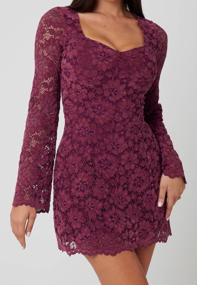 Femme portant une robe bordeaux moulante en dentelle florale à manches longues avec un décolleté carré et un ourlet et des poignets festonnés.