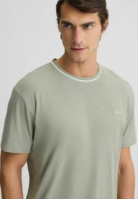 T-shirt verde chiaro a maniche corte con colletto tondo, caratterizzato da una finitura bianca a contrasto e un piccolo logo ricamato sul lato sinistro del petto.