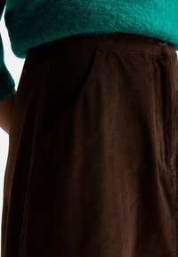 Hnědá kordrová sukně s bočními kapsami, texturovanou tkaninou a vysokým pasem. V kombinaci s teal pleteným svetrem pro kontrast.