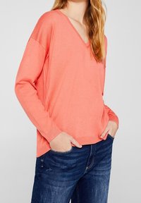 Koraalvink trui gemaakt van zacht materiaal, met lange mouwen en ribbelmanchetten, gecombineerd met donkere jeans, met een ontspannen pasvorm.