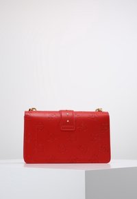 Borsa a mano in pelle rossa con chiusura a pattina sicura, hardware color oro e dettagli di branding sottili. Presenta una forma strutturata.