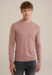 Suéter de punto rosa claro con mangas largas, cuello redondo y puños y dobladillo acanalados. Lleva puesto un pantalón vaquero gris oscuro. Textura suave.