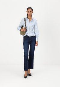 Blå og hvit stripete skjorte med rynkede sider, kombinert med mørkeblå breddejeans og svarte lakkhæler. Olivengrønn skulderveske.