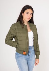 Zielona oliwkowa kurtka puchowa z zamkiem z przodu, ściągaczami na mankietach i u dołu. Posiada pikowaną fakturę oraz pomarańczową metkę marki na lewym biodrze.