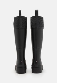 Bottes de pluie en caoutchouc noires avec une partie supérieure texturée. Elles disposent d'une semelle plate, d'une languette et d'un petit détail rayé à l'arrière.