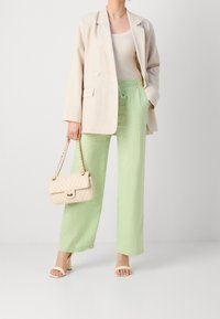Béžový lněný blejzr, přiléhavý krémový top na ramínka, světle zelené široké kalhoty a béžová prošívaná kabelka. Sandály s otevřenou špičkou a blokovým podpätkem.