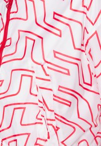 Bílá lehká bunda s červeným geometrickým vzorem, se zipem vpředu a bočními kapsami. Hladký povrch s lesklým finish.