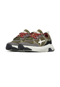 Une paire de baskets vert olive, grises et noires avec des lacets rouges et des semelles blanches, arborant un logo croix blanc sur le côté.